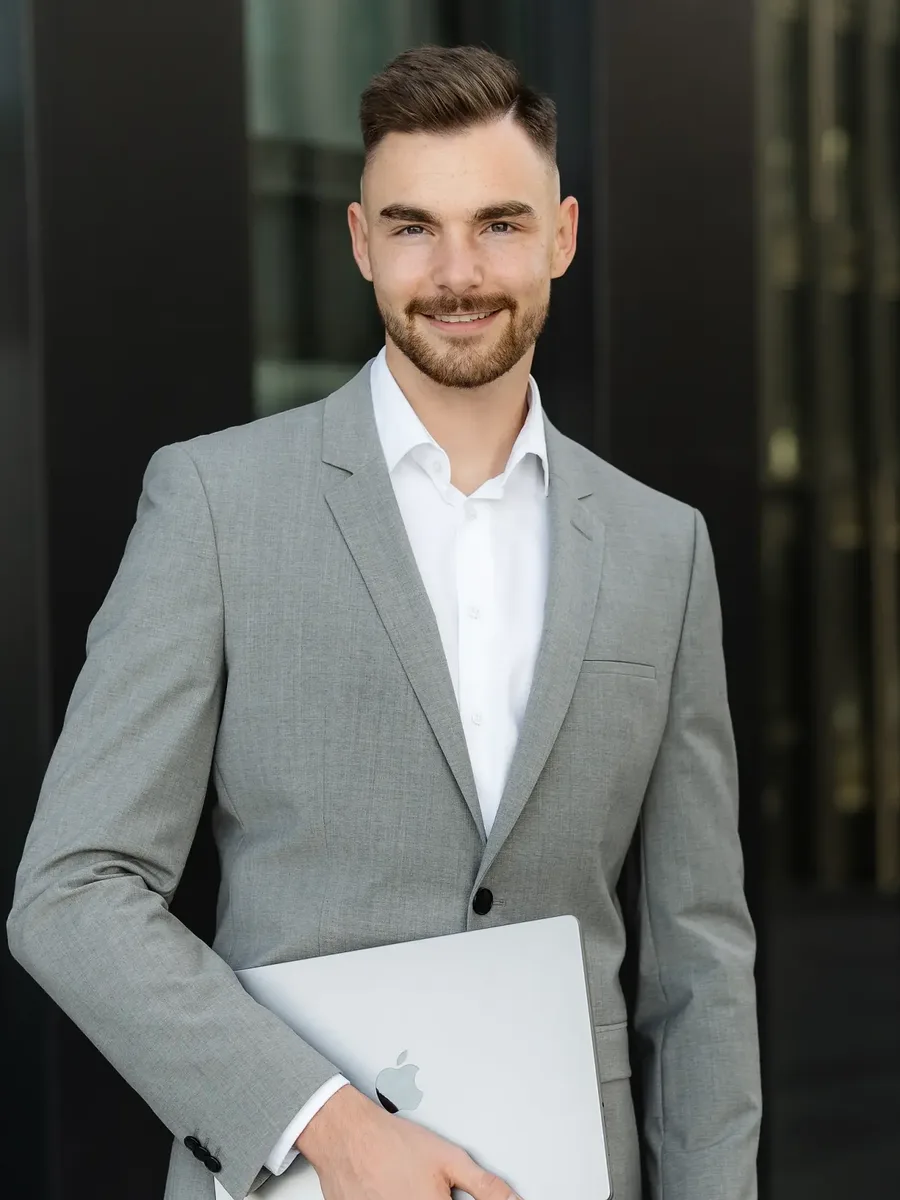 Jan Philipps, Google-Ads-Freelancer, mit MacBook unter dem Arm vor einer dunklen Glasfassade