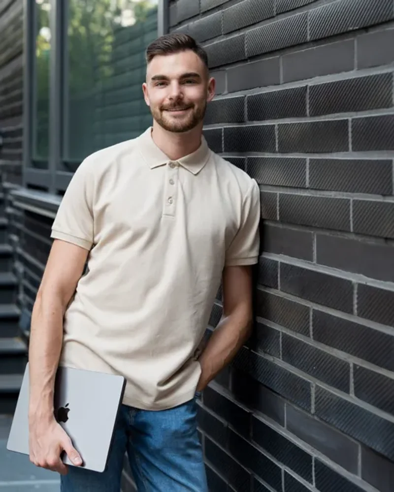 Jan Philipps mit dem MacBook unter dem Arm vor einer dunklen Backsteinwand